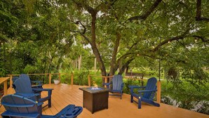 An outdoor deck with wooden flooring, surrounded by lush greenery and trees. - Riverside Cottage just a short walk to downtown! (Bonita Springs)