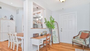A room with a wooden dining table, white chairs, a white cabinet, a mirror, a plant, and a vintage armchair. - Riverside Cottage just a short walk to downtown! (Bonita Springs)