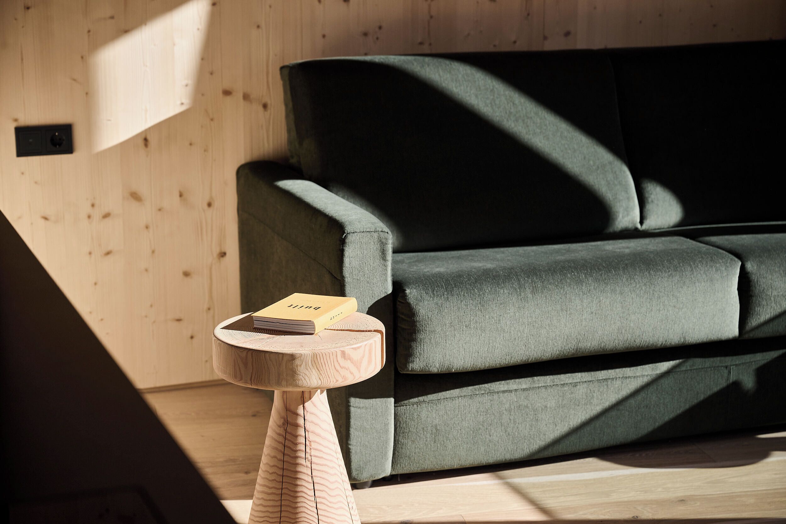 A modern room with a wooden floor, a green sofa, and a small wooden side table with a book on it.