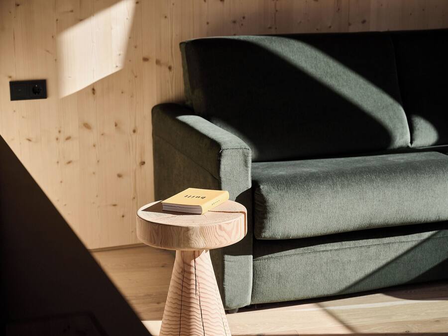 A modern room with a wooden floor, a green sofa, and a small wooden side table with a book on it.