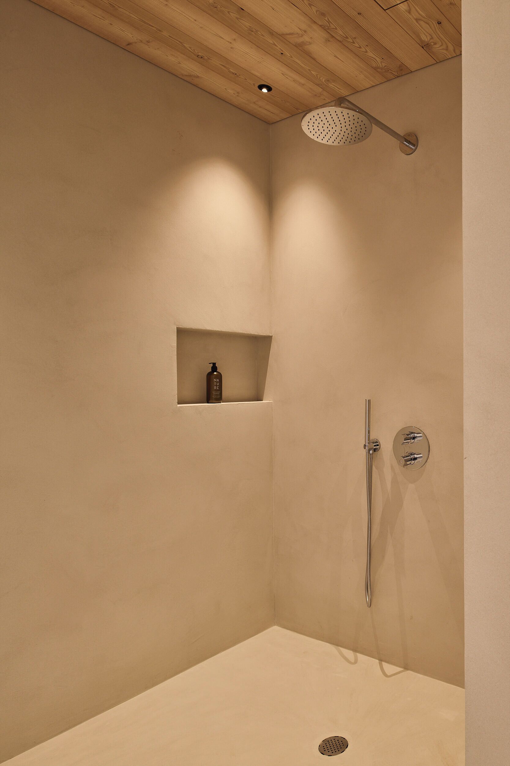 A shower with a handheld showerhead, a wall-mounted faucet, and a small shelf with a bottle.