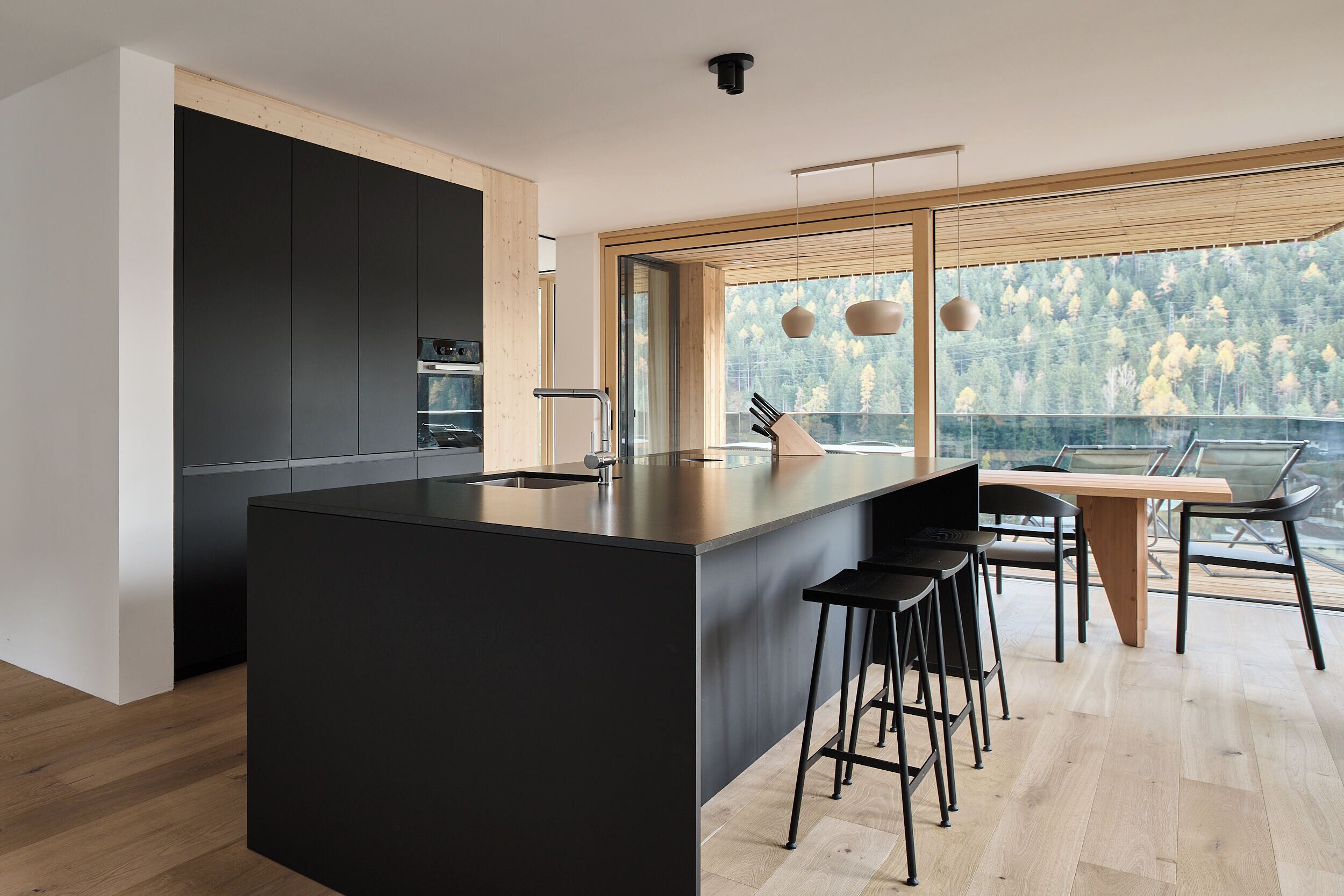 Una cocina moderna con una isla central, taburetes de bar y un amplio ventanal con vistas a árboles.