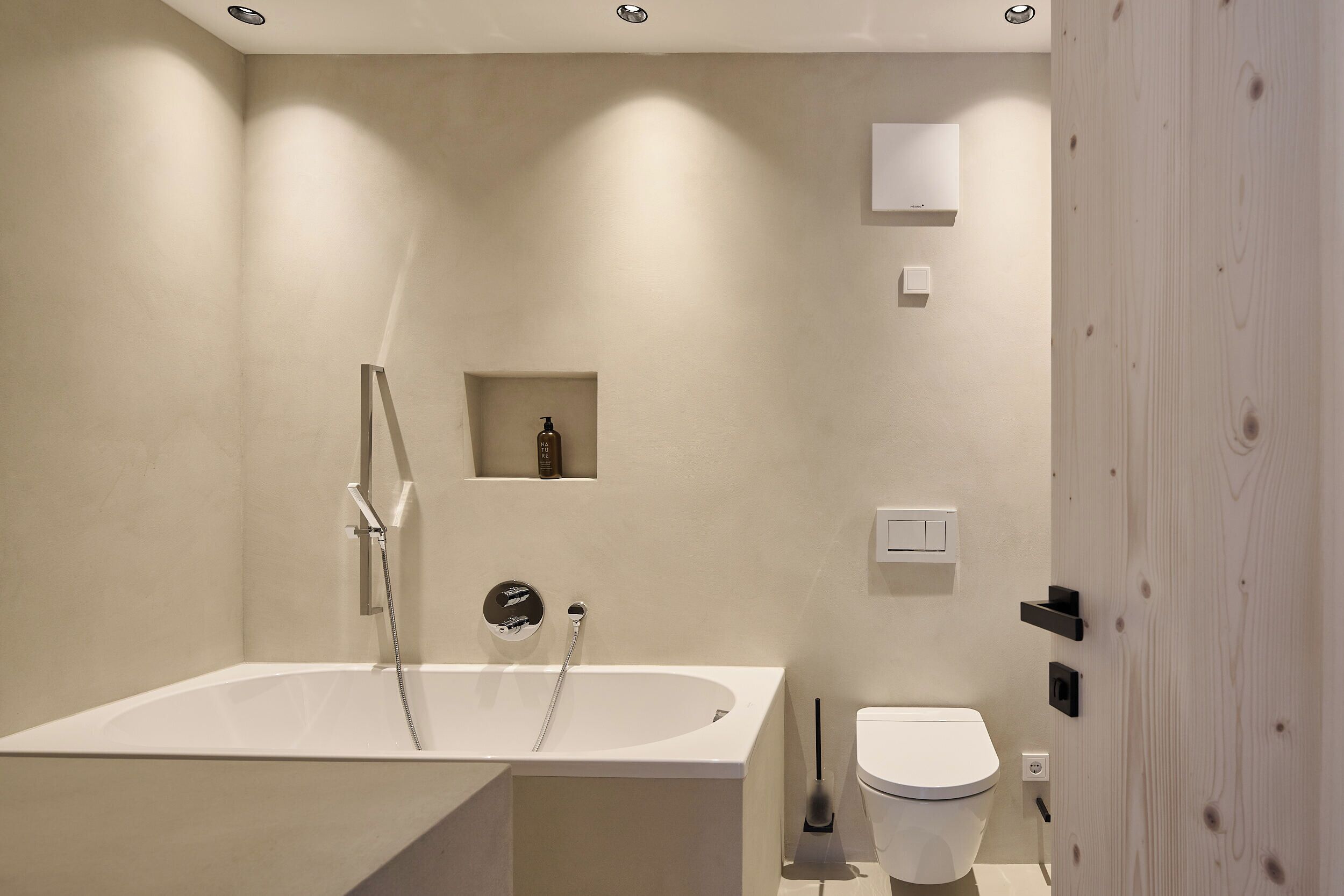 Ein modernes Badezimmer mit einer freistehenden Badewanne, einer Toilette und einem kleinen Ablagebereich für Pflegeprodukte.