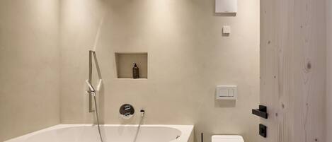 Ein modernes Badezimmer mit einer freistehenden Badewanne, einer Toilette und einem kleinen Ablagebereich für Pflegeprodukte.