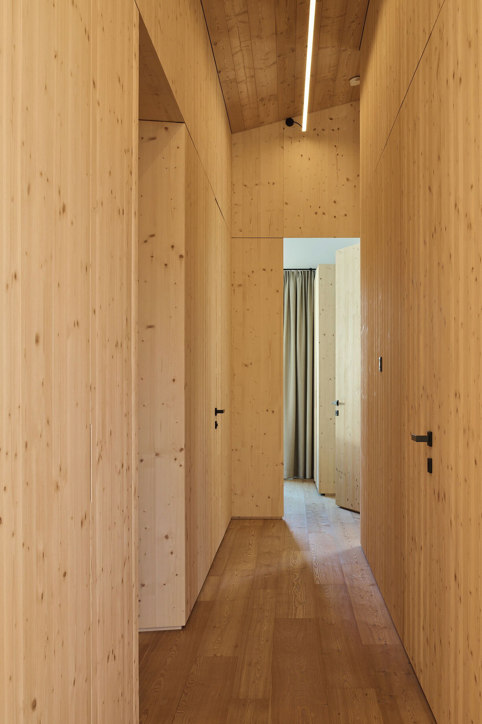 A narrow hallway with wooden walls and a wooden floor, leading to a room with a curtain.