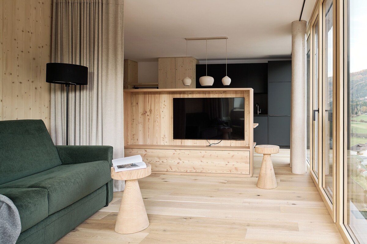Un salon moderne avec un canapé vert, une table basse en bois et un coin cuisine doté d’une grande fenêtre.