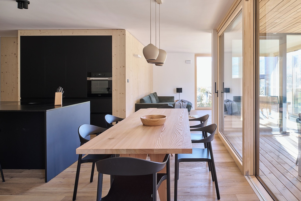 A modern kitchen with a wooden island, black cabinetry, and a dining area with a wooden table and chairs.