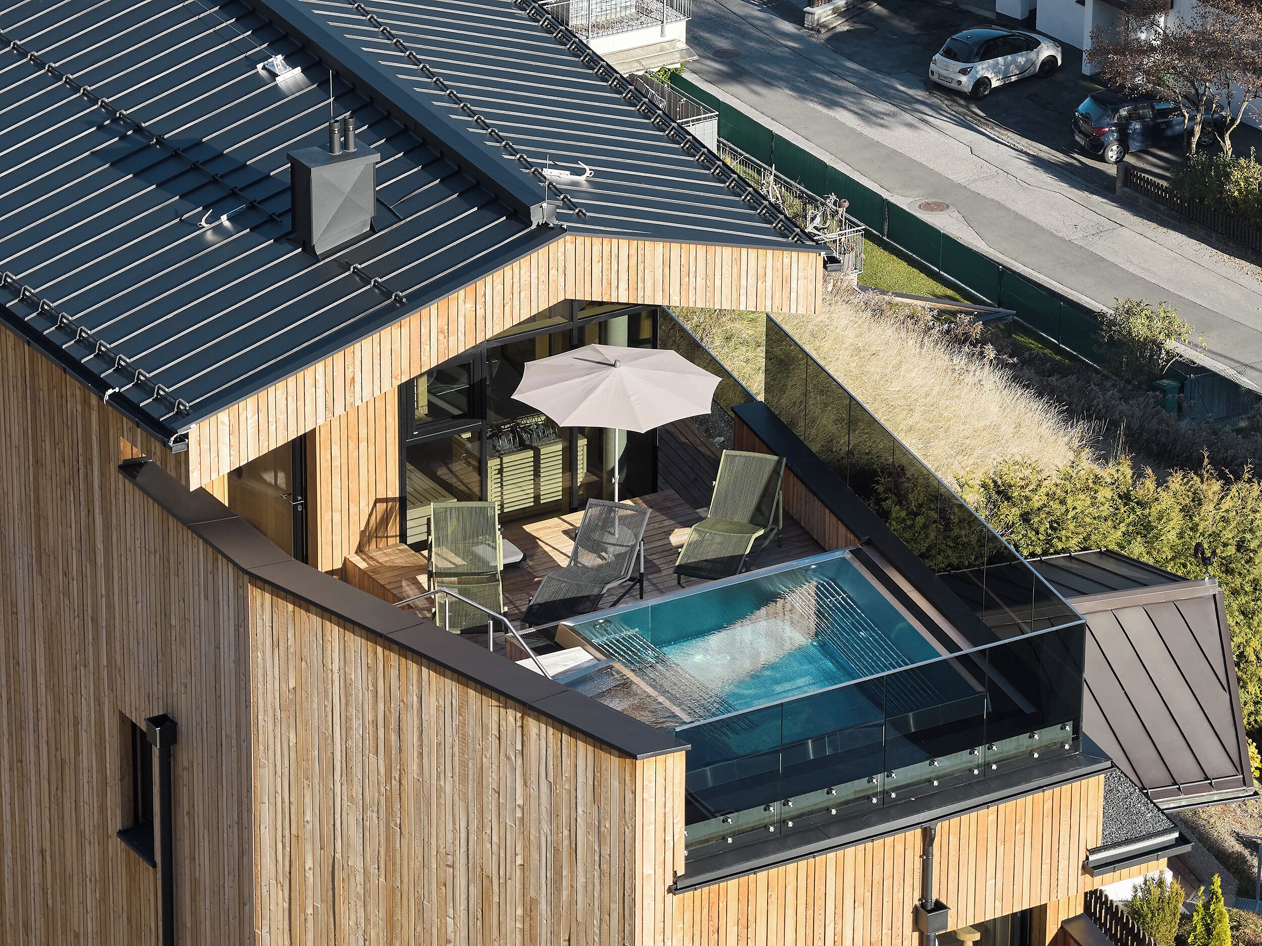 Een modern gebouw met een zwembad op het dak, een houten gevel en een glazen balkon met buitenmeubilair.