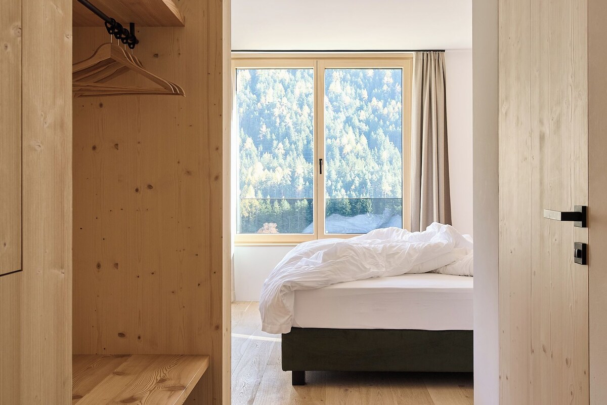 Une chambre à coucher avec un lit, une armoire en bois et une grande fenêtre donnant sur des arbres.