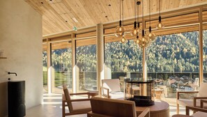 A modern interior with large windows, wooden furniture, and a view of a forested mountain. - Lärchenlodge SkySpa und Rooftop Pool (Fulpmes)