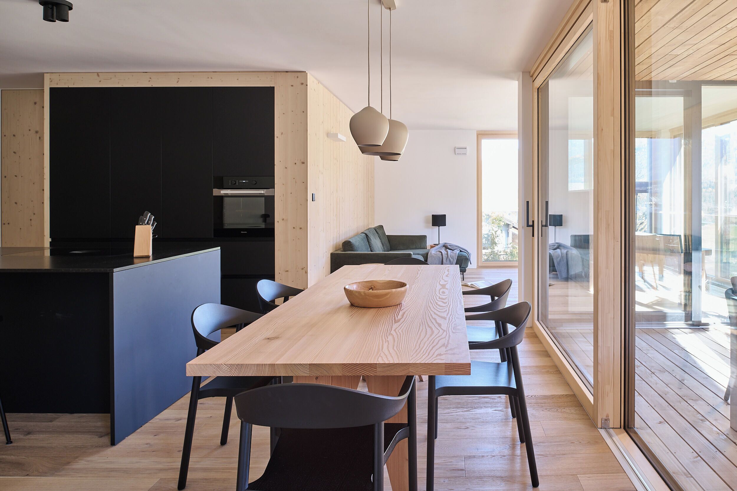 A modern kitchen with a wooden island, black cabinetry, and a dining area with a wooden table and chairs.