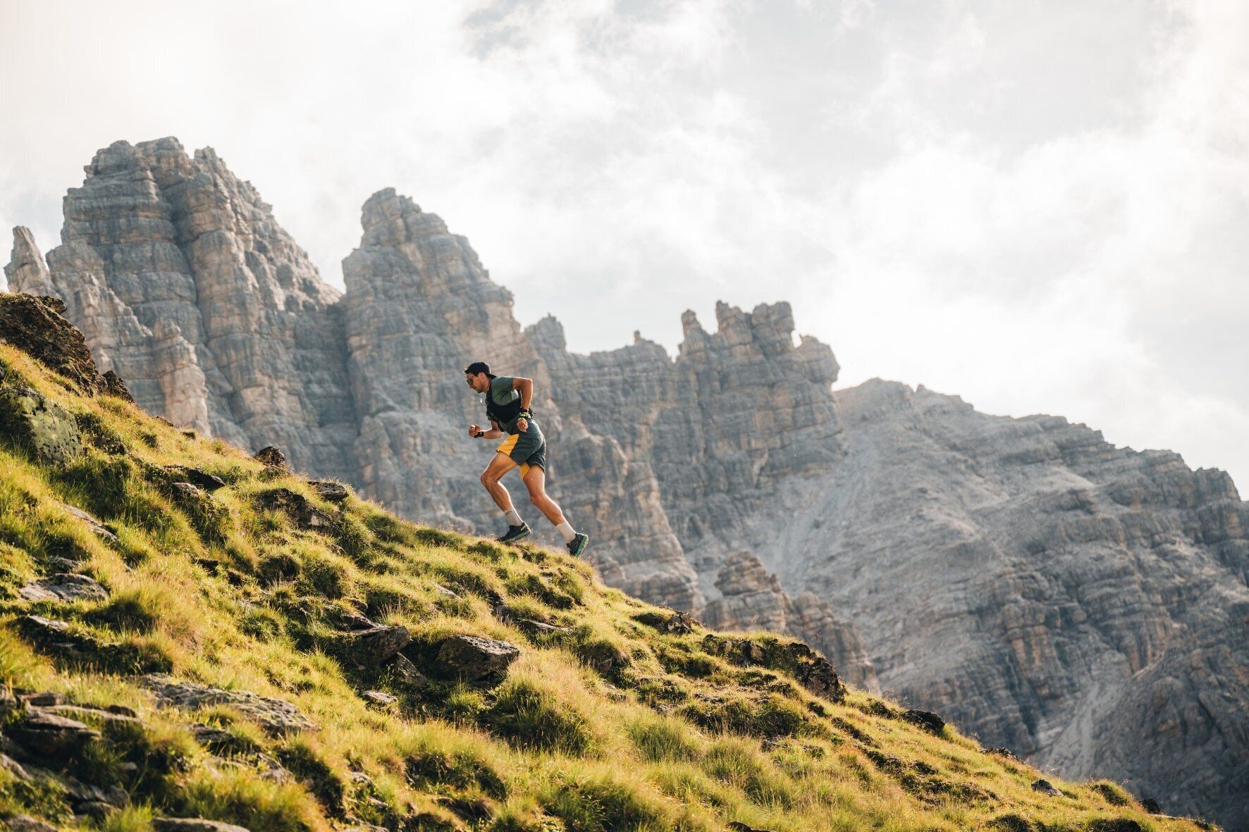 A person running on a grassy hill with rocky cliffs in the background.