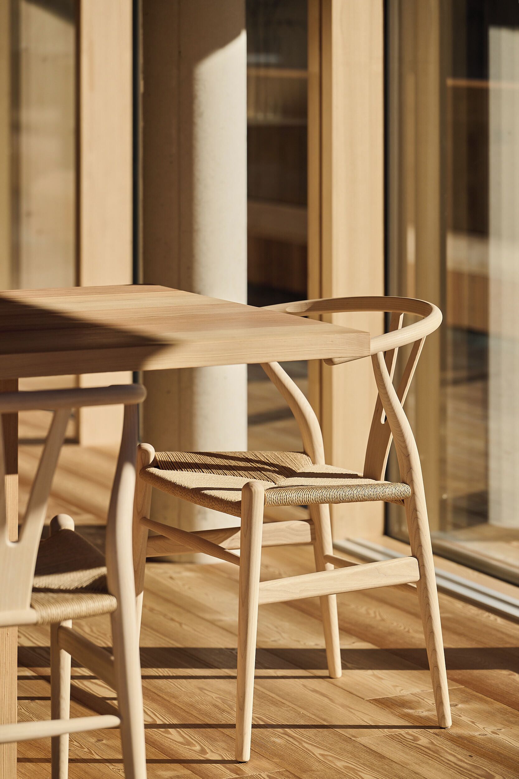 A wooden table and chair set in a room with large windows and wooden flooring.