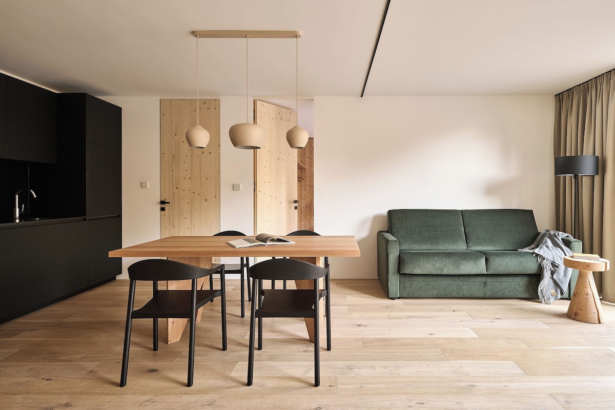 A modern living space with a wooden dining table, black chairs, a green sofa, and a wooden floor.