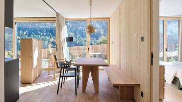 A modern interior with a wooden dining table, chairs, and a bench. There is a large window with a view of a forested area.