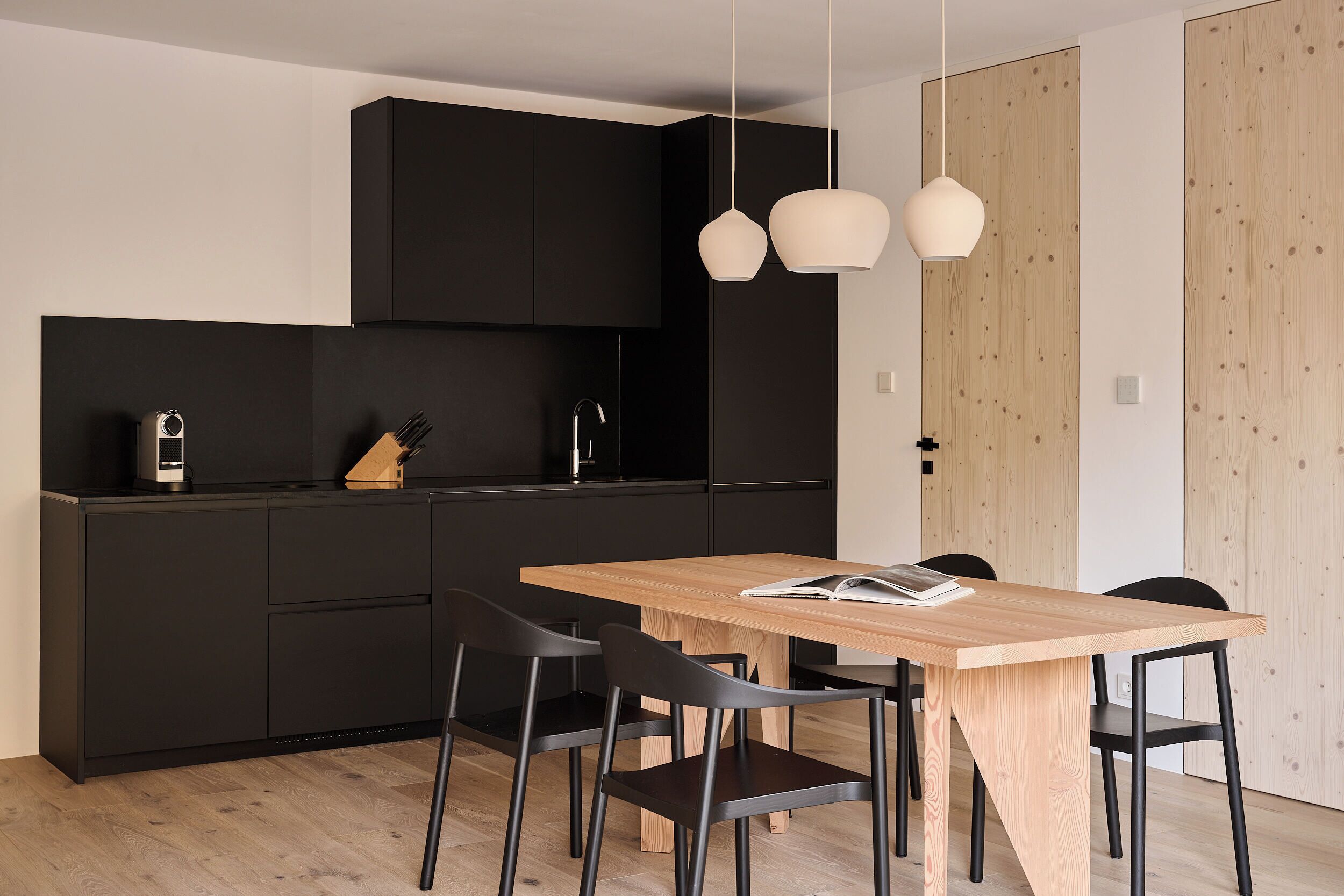A modern kitchen with dark cabinetry, a wooden dining table, and black chairs.