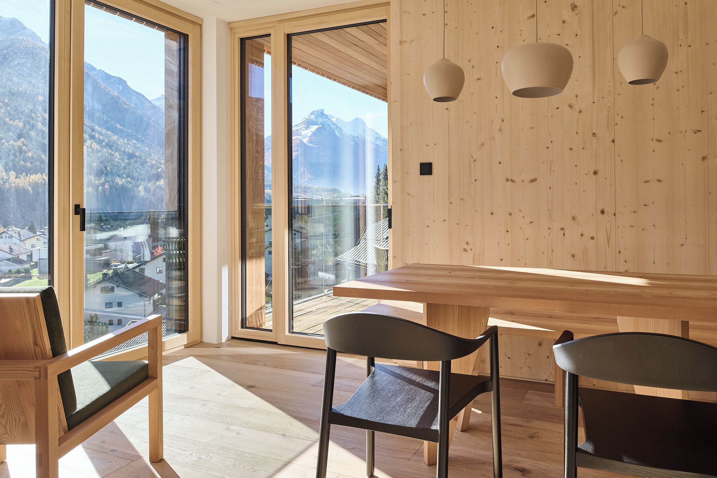 Un interior moderno con una mesa de madera, dos sillas y un amplio ventanal con vistas a la montaña.
