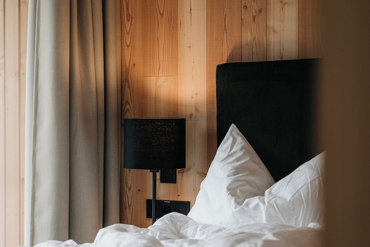 Un lit bien fait, avec du linge de lit blanc, une tête de lit noire et une lampe de chevet.