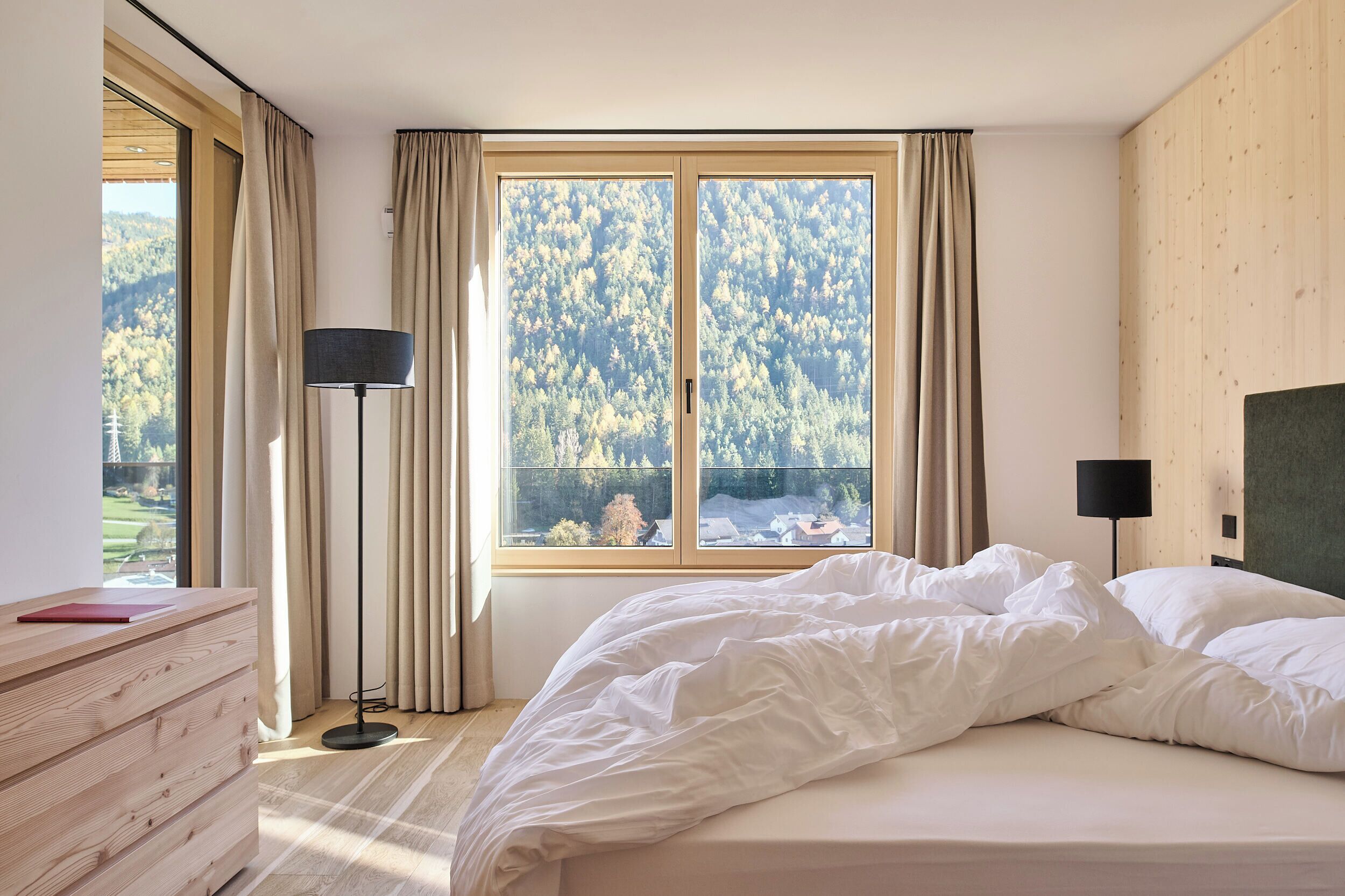 Una camera da letto con un'ampia finestra, una lampada da comodino e un comò in legno.