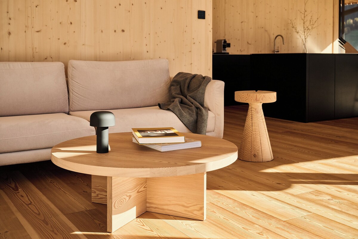 Un salon moderne avec une table basse ronde en bois, un canapé et une petite table d’appoint en bois.