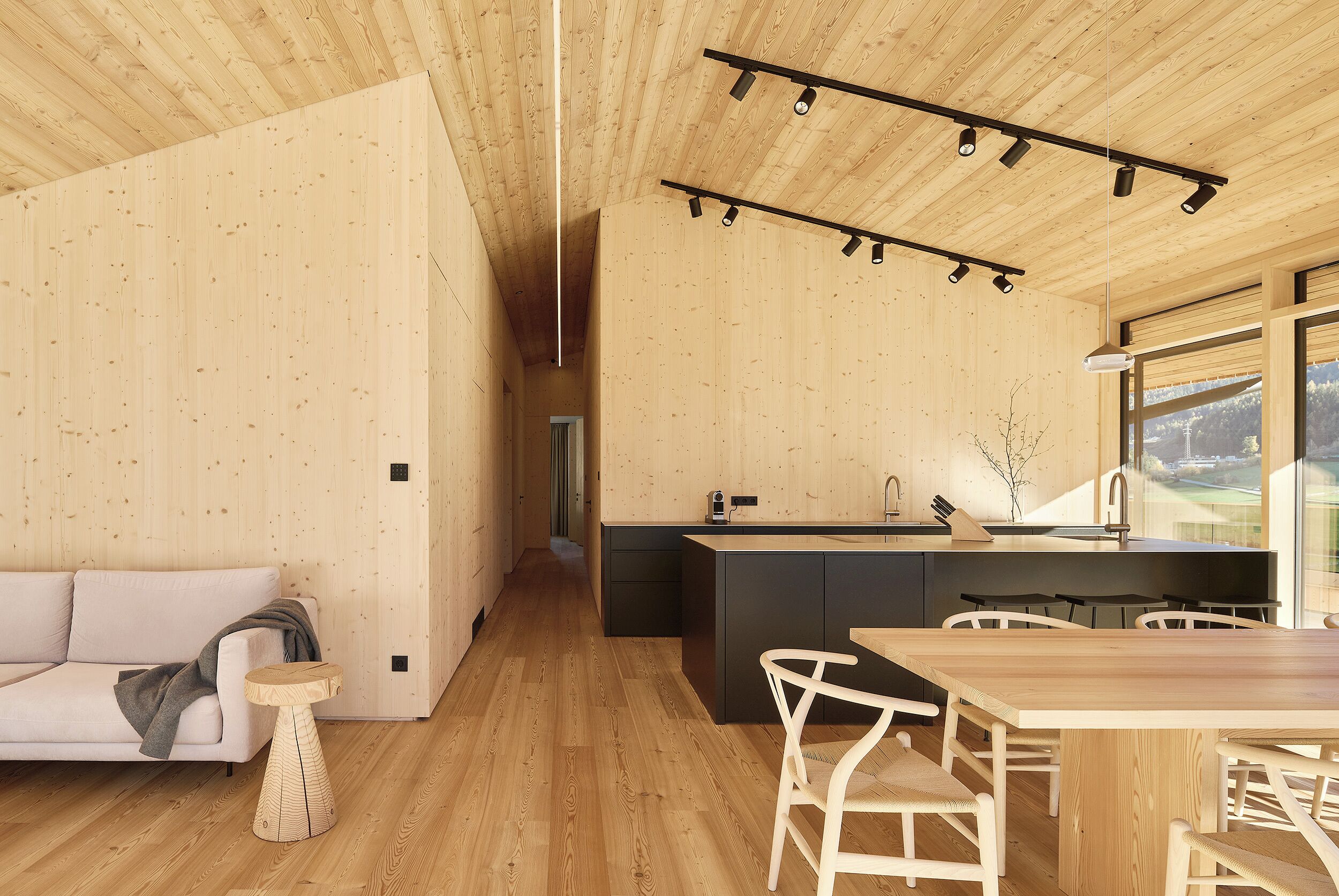 A modern interior with a wooden ceiling, a kitchen area with a large island, and a dining space with white chairs.