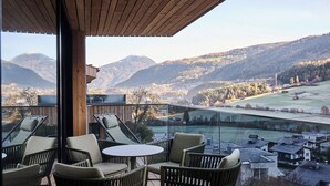 A balcony with wicker chairs and a table, overlooking a valley with mountains and a river. - Lärchenlodge SkySpa und Rooftop Pool (Fulpmes)