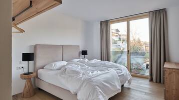 A bedroom with a bed, a bedside table with a lamp, a wooden headboard, a window with curtains, and a view of the outside.