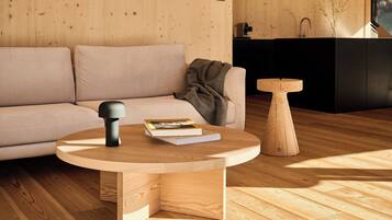 A modern living room with a round wooden coffee table, a sofa, and a small wooden side table.