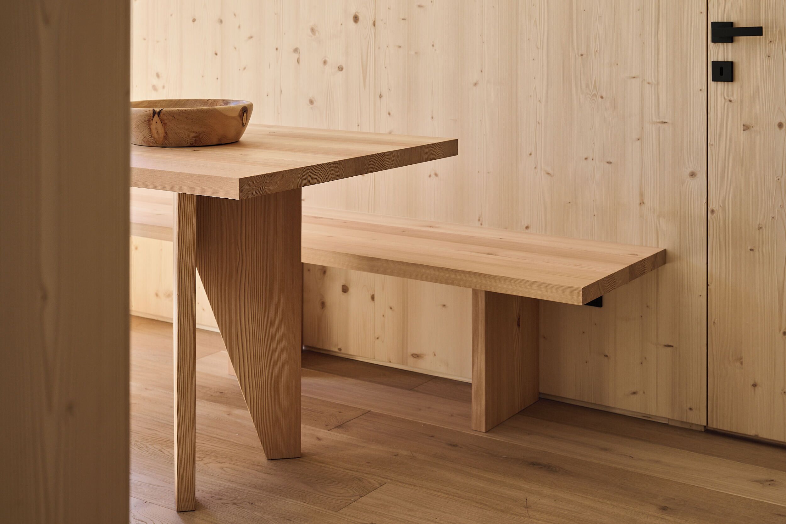 Una mesa de madera con un bol, un banco y una puerta con manija.