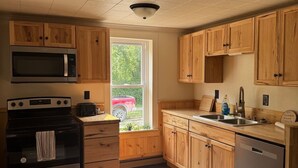 Une cuisine avec des meubles en bois, des appareils électroménagers en acier inoxydable, une fenêtre et une vue sur une voiture rouge garée à l’extérieur.