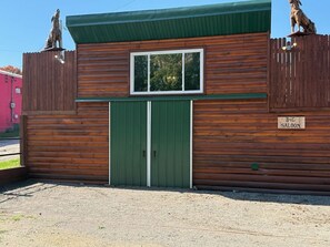 A wooden building with a green door and window, a sign reading 'B&G SALOON,' and a fenced area. - Historical Stone and Log Cabin (Paris)