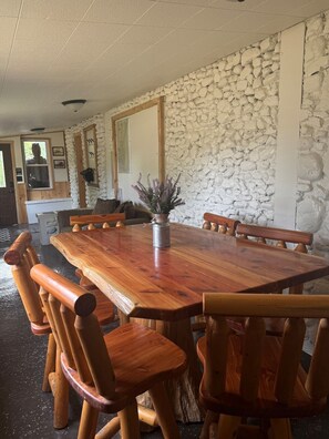 A wooden dining table with chairs, a stone wall, and a window with a view. - Historical Stone and Log Cabin (Paris)
