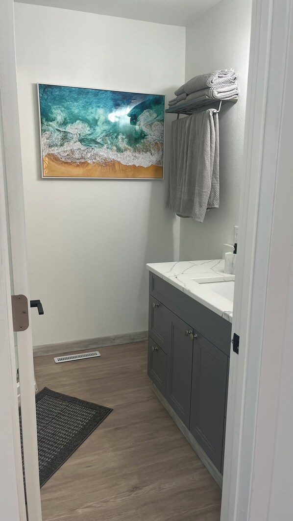 Un baño con piso de madera, un lavamanos blanco y un perchero para toallas.