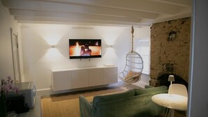 A modern living room with a television mounted on the wall, a green sofa, a hanging chair, and a small white table. - Bosch Huis Rosé • Central • VIP • Parking (Savannah)