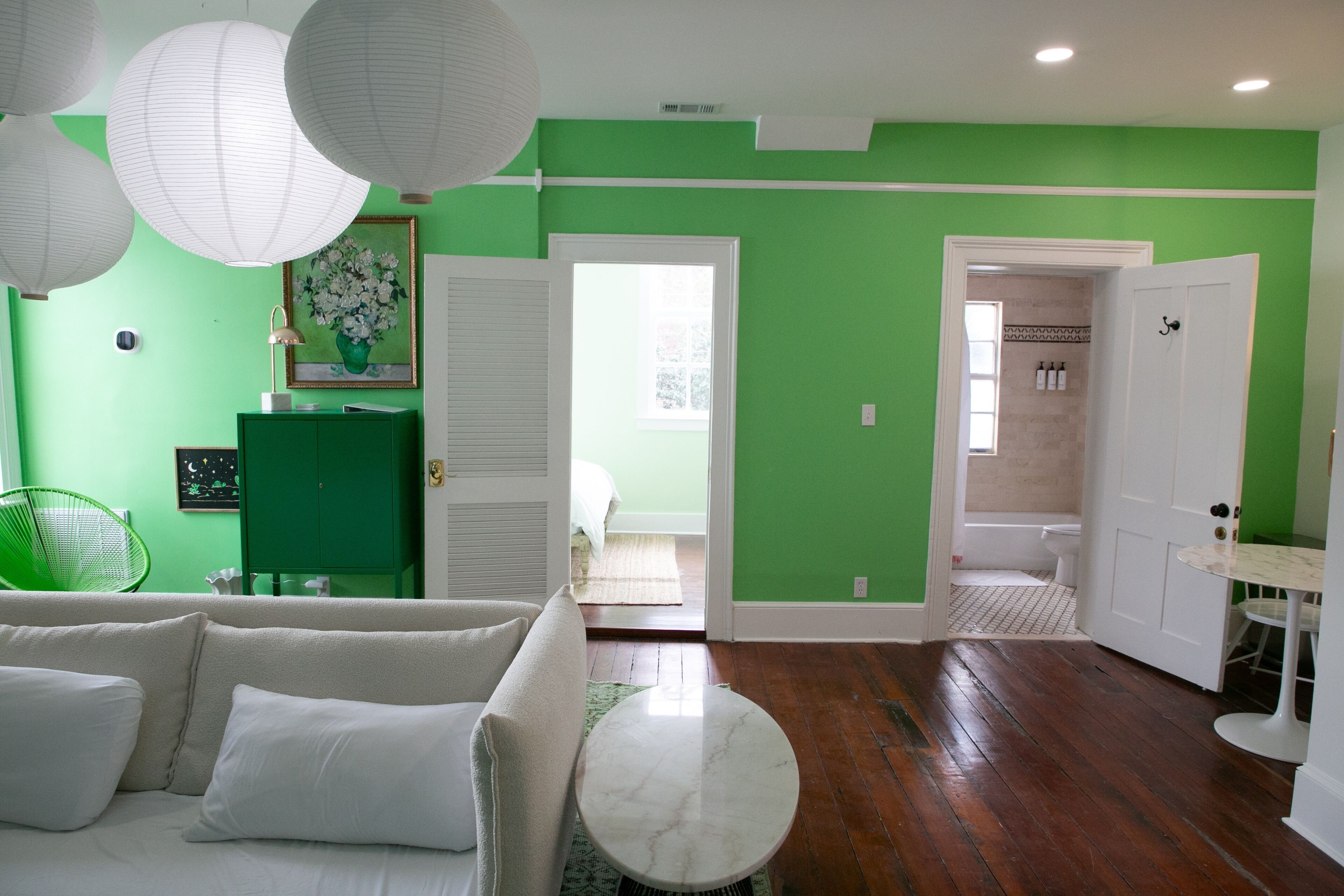 Quarto com parede verde, móveis brancos, um armário verde e um banheiro visível por uma porta aberta.