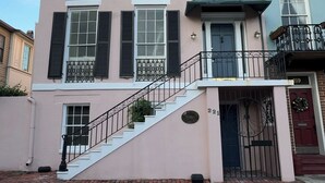 A multi-story building with a pink facade, black shutters, and a green awning. - Bosch Huis Rosé • Central • VIP • Parking (Savannah)