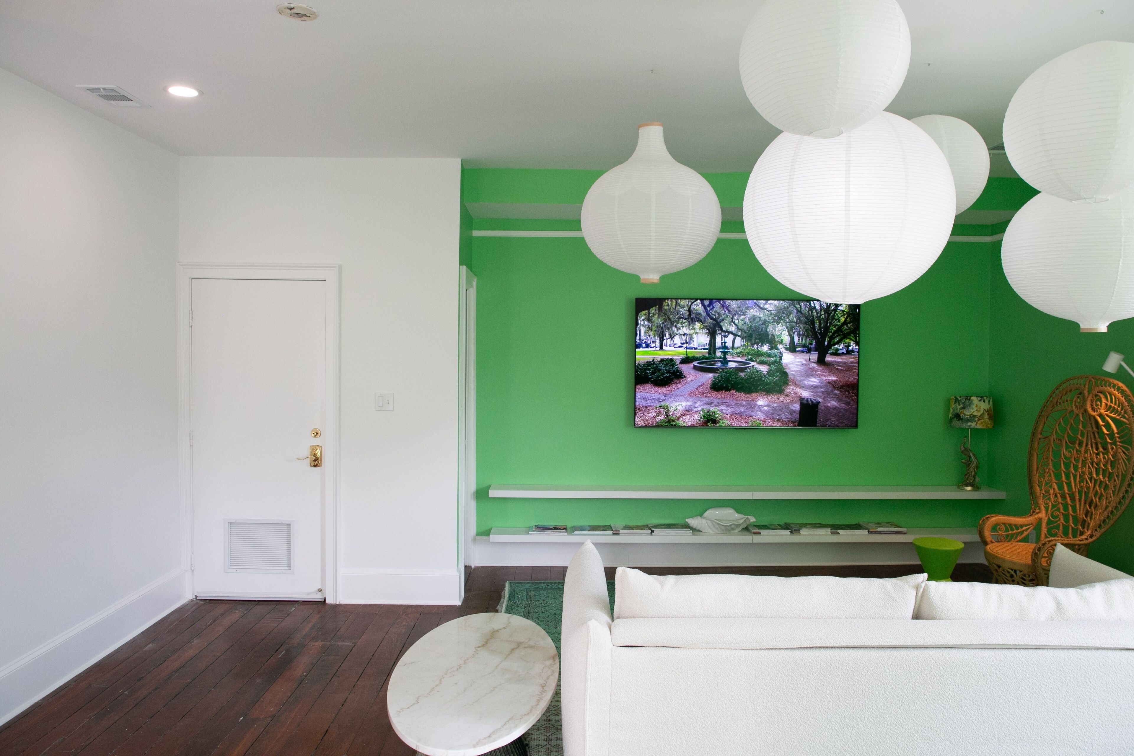A living room with a green accent wall, a television mounted above a bench, and a white sofa with a round coffee table.