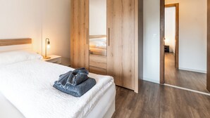 A bedroom with a bed, a wooden wardrobe, a nightstand with a lamp, and a bathroom visible through an open door. - Fabi s Horu Lodge (Zermatt)