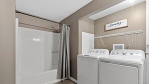 Zona de lavandería con lavadora y secadora, ducha con cortina y un perchero para toallas.