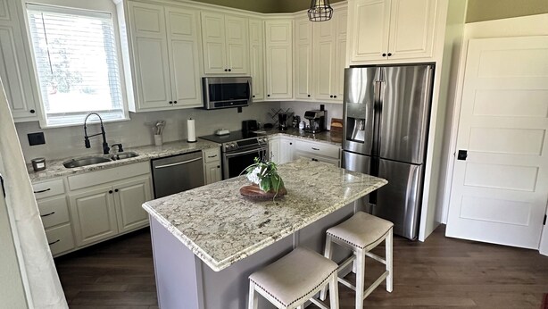 A modern kitchen with white cabinets, a granite countertop island with two stools, stainless steel appliances, and pendant lighting. - THE BUNK HOUSE (Rock Spring)