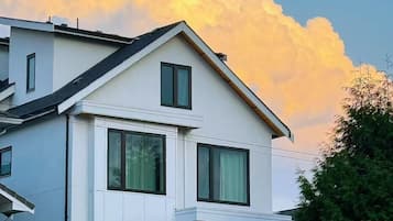 Ein modernes, zweistöckiges Haus mit flachem Dach, großen Fenstern und einer kleinen Veranda.