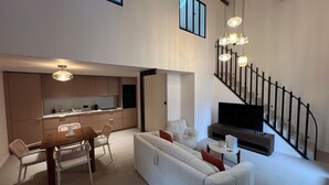 Un espace de vie moderne comprenant un coin repas, un canapé, un téléviseur, un escalier et une cuisine.