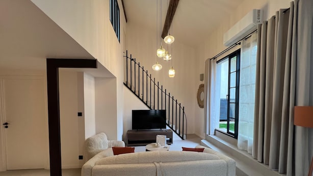 Un salon moderne avec un escalier, un téléviseur à écran plat et une grande fenêtre agrémentée de rideaux.
