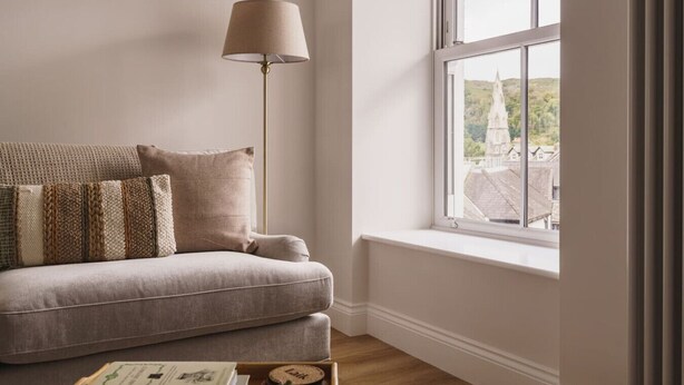 Et værelse med sofa, gulvlampe og et vindue med udsigt til en bygning.