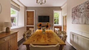 Ein Esszimmer mit Holztisch, Stühlen, einer Deckenleuchte, einem Fernseher und einem Heizkörper.