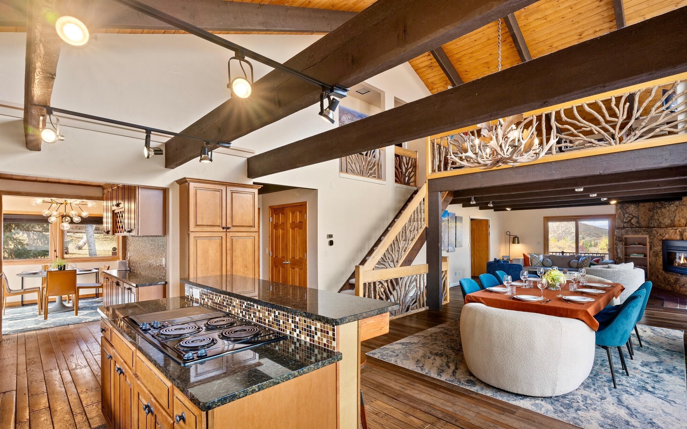A spacious kitchen with a large island, wooden beams, and a dining area with blue chairs and a table set for four.