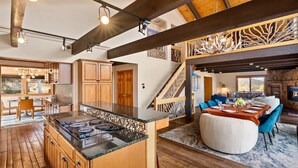 Una cocina amplia con una isla grande, vigas de madera y un comedor con sillas azules y una mesa preparada para cuatro.