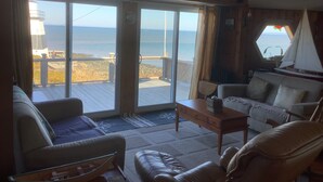 Un salon confortable avec une grande porte-fenêtre coulissante donnant sur une terrasse avec vue sur l’océan. On y trouve un canapé, une table basse et un fauteuil.