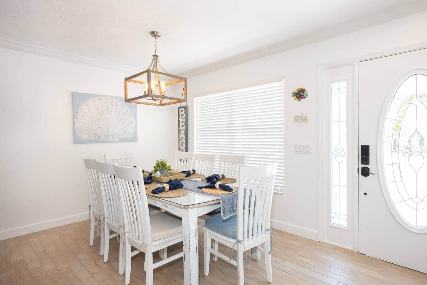 Un coin repas avec une table blanche, des chaises blanches, un lustre et une porte ornée d’un vitrail.