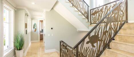 A staircase with a decorative railing featuring animal silhouettes, a light-colored interior, and a hallway leading to a room with a large window.